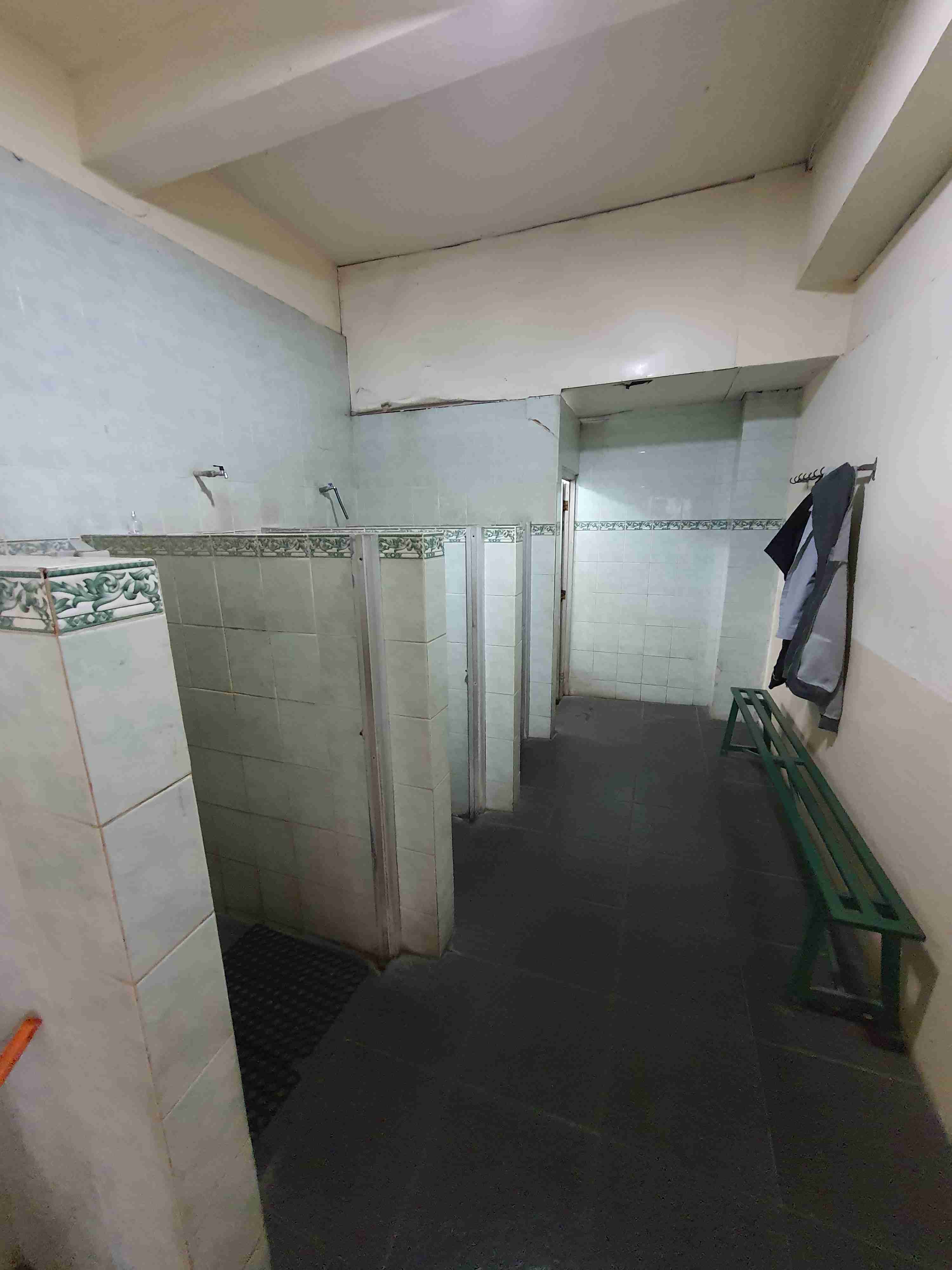 Foto kamar mandi pria yang bersih dengan beberapa bilik untuk mandi.